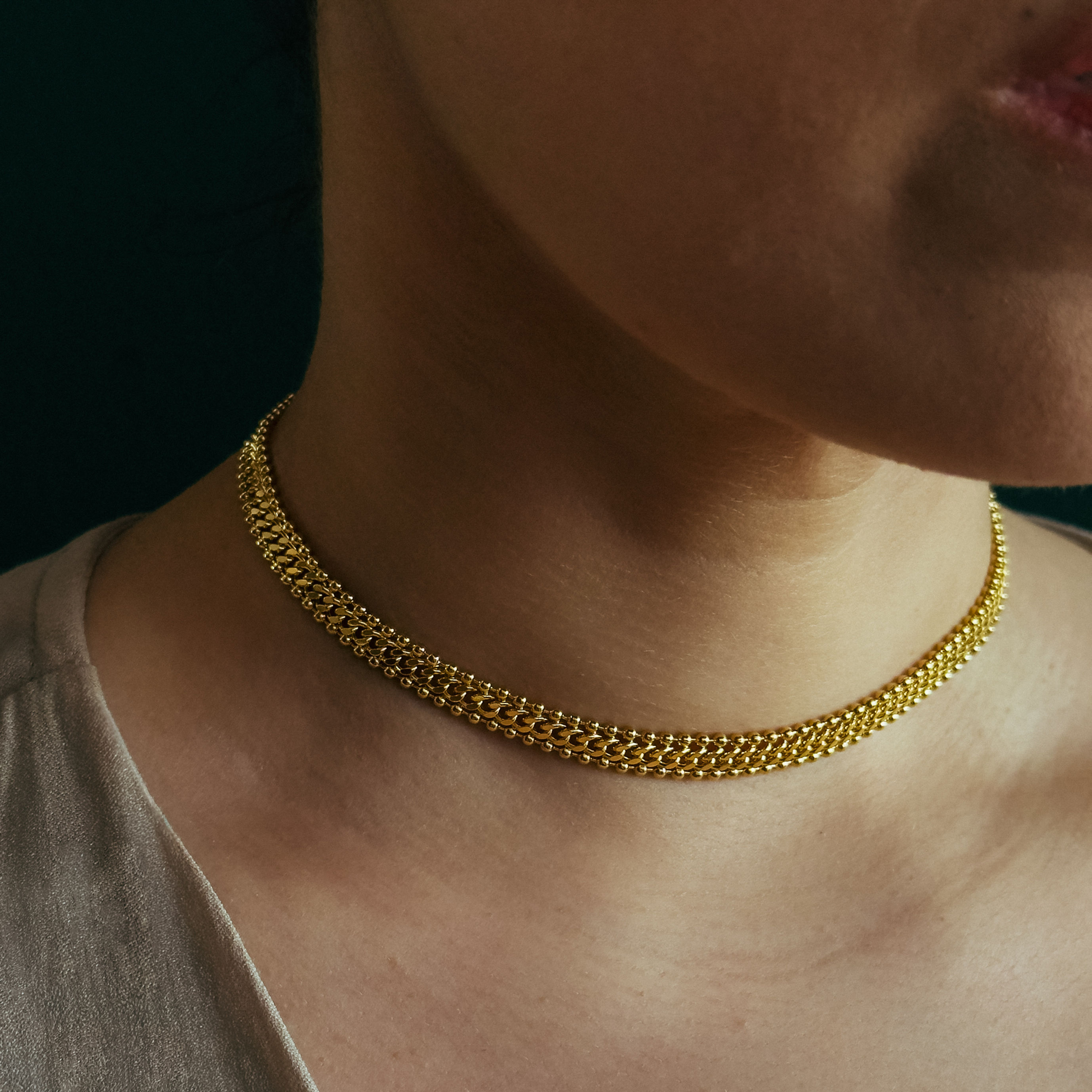 Colar em banho de ouro, corrente curta de trama entrelaçada e fecho com extensor para ajuste de tamanho.