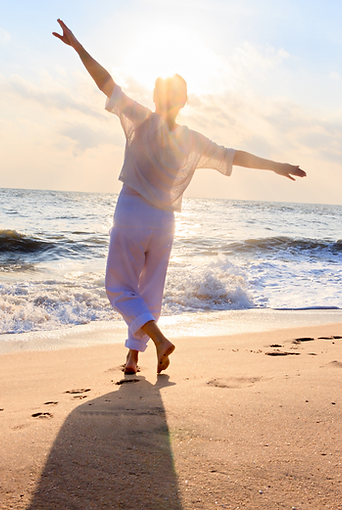 women on beach with the sun behind her dancing with her hands in the air with happiness