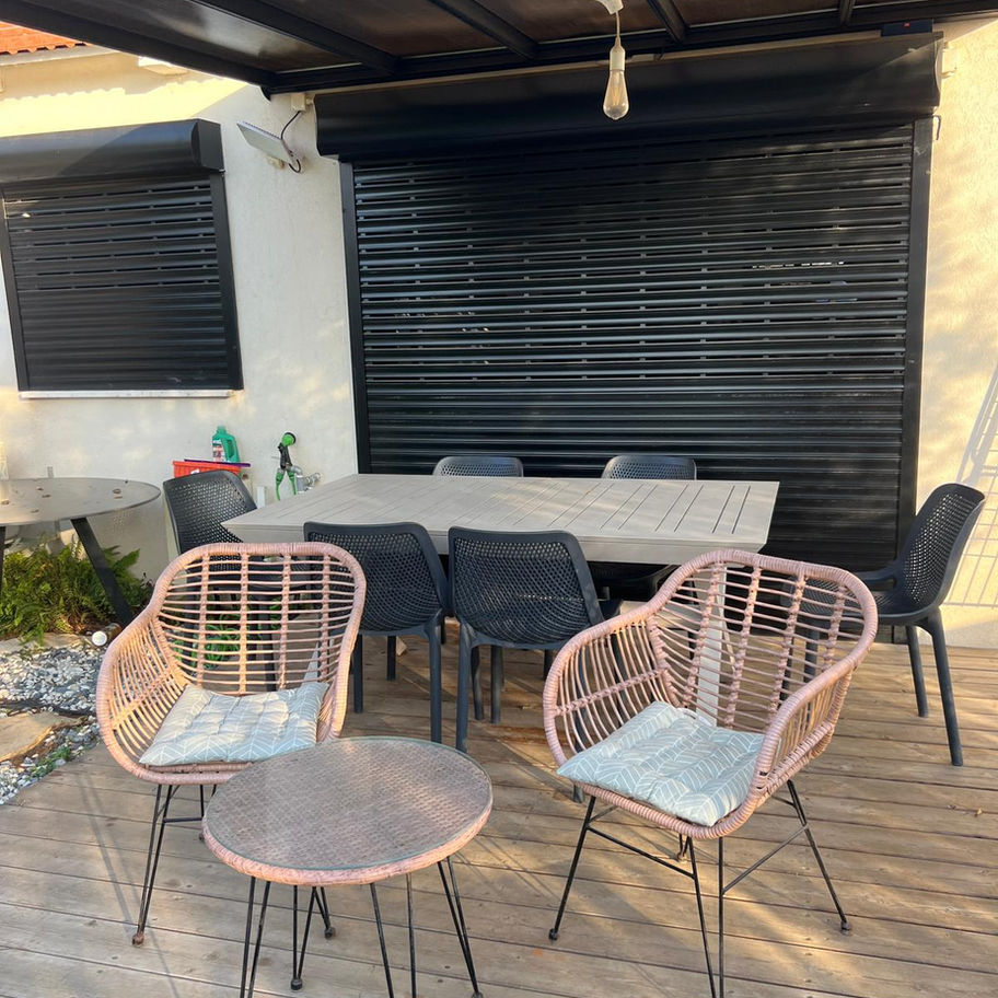 דק עם 2 כיסאות קש ושולחן וברקע יש תריס שחור סגור