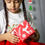Thumbnail: A curious girl wearing a t shirt from Hugs&Hues having Merry Christmas embroidered on it and holding a gift