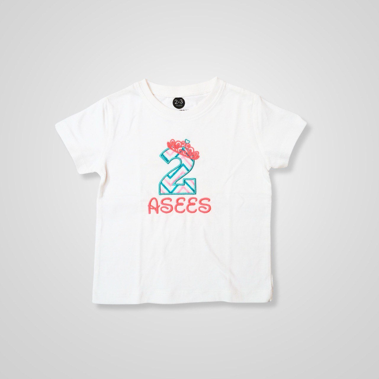 a photo of a t shirt by Hugs&Hues having number 2, a name and a tiara/crown embroidered on it