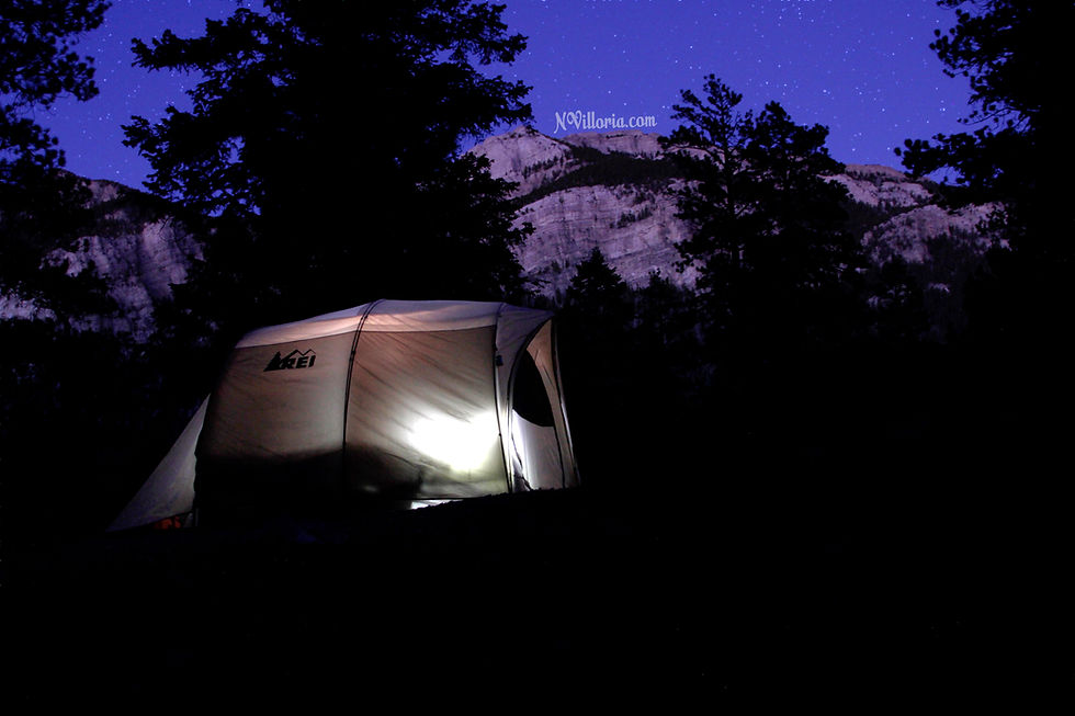 an illuminated tent in the woods at night. in the background mountains and trees cna be seen