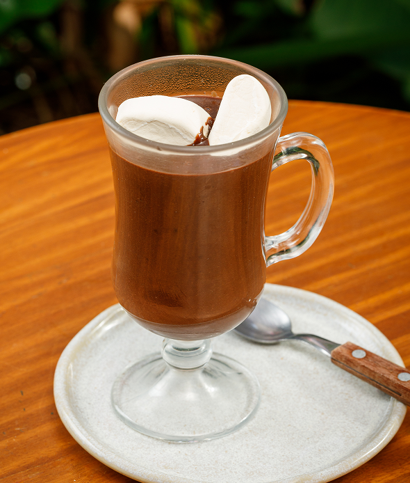 Chocolate quente cremoso servido com marshmallows em caneca de vidro.