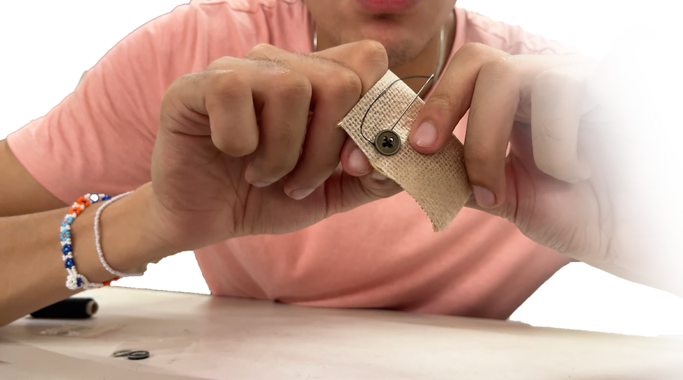 A person in a pink shirt sewing a button onto beige fabric. Close-up of hands and needle. Colorful beaded bracelet visible on wrist.