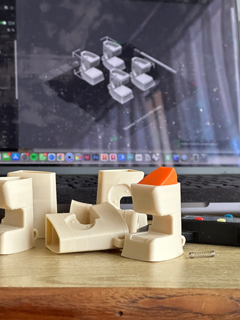Multiple 3D-printed white components arranged on a table near a laptop, showing iterative enclosure and part design.
