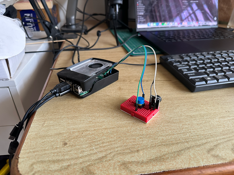 Raspberry Pi with cables on a desk, connected to a red breadboard with blue and black wires. Laptop and keyboard in the background.