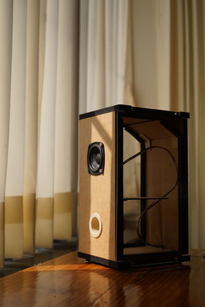 Speaker box with a speaker in a windowed room with curtains.