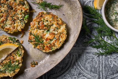 Golden herb and crab cakes with lemon and dill on a rustic metal pan, cookbook food photography