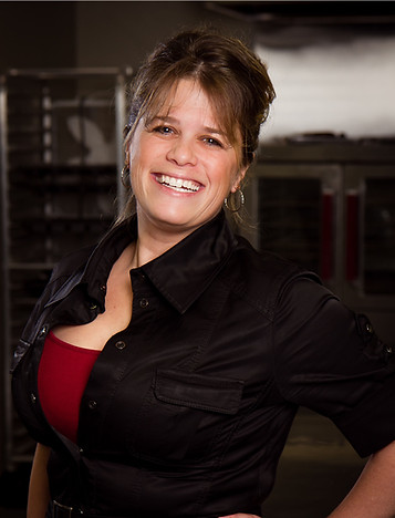 amanda loren smiling at camera in a commerical kitchen with black dress and red top on.
