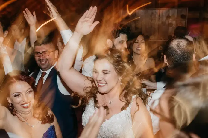 DJ Dan Fudim, NYC DJ, at a lively wedding reception, entertaining guests who are dancing energetically and raising their hands in celebration.