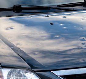 Black car engine hood with many hail damage dents show the forces of nature and the import