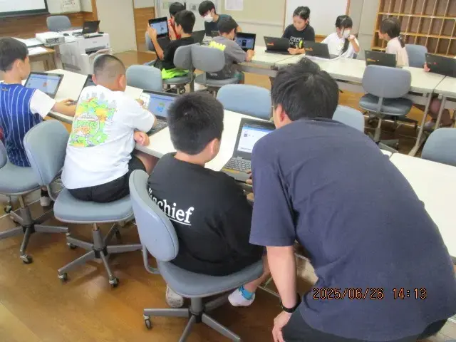 パソコンで作業している生徒に教師が後ろからアドバイスをしている