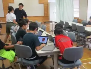 パソコンで作業している生徒に後ろからアドバイスをしている