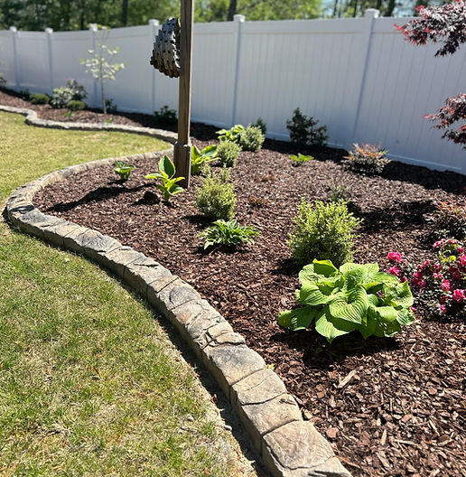 Curved natural stone concrete landscape curbing bordering a mulched garden bed with plants and flowers