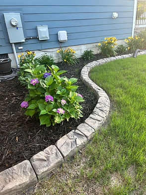 Decorative natural stone concrete curbing following a sweeping curve around a mulched flower bed with blooming hydrangeas