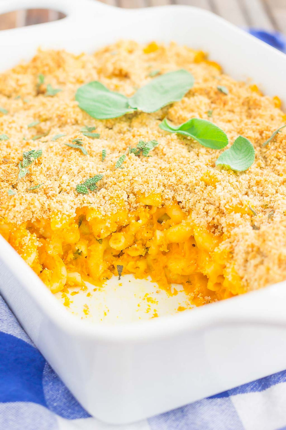 pumpkin mac and cheese in a white casserole dish topped with sage.
