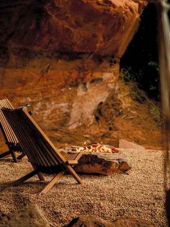 two wood lounge chairs sitting next to a fire pit against a red rock wall at Cave Lakes in Kanab, Utah.