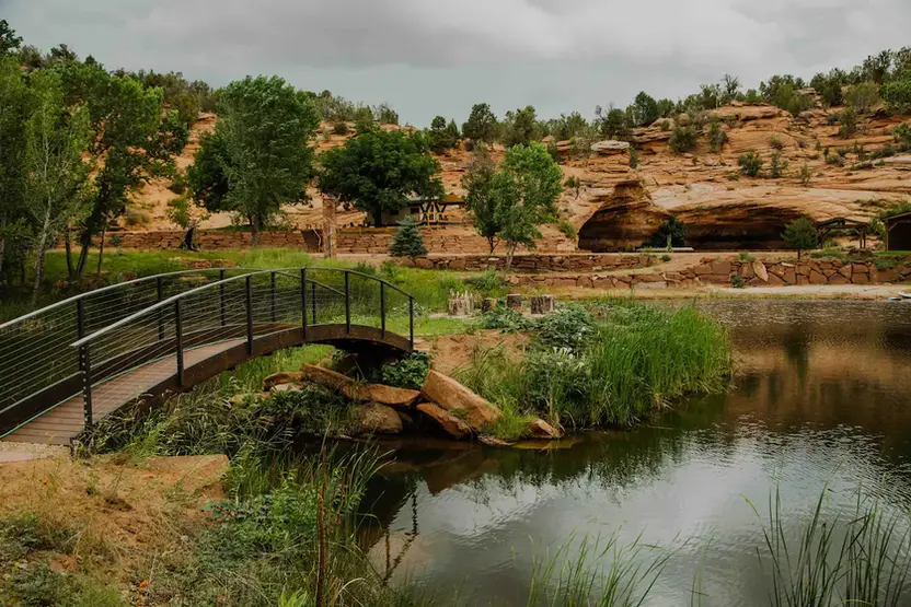 Wooden footbridge crossing a scenic pond surrounded by red rock desert landscapes at a Zion glamping resort.