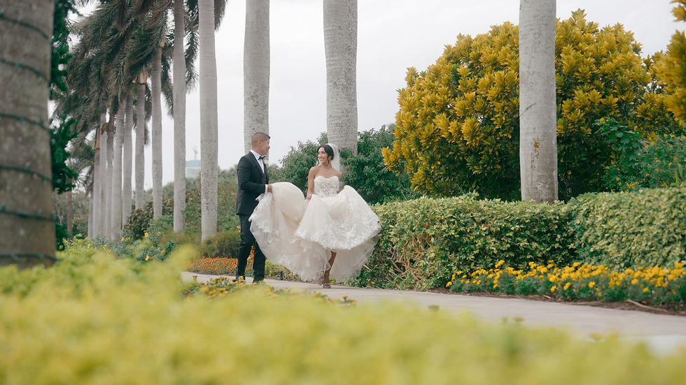 groom holds bride's wedding dress walking in garden