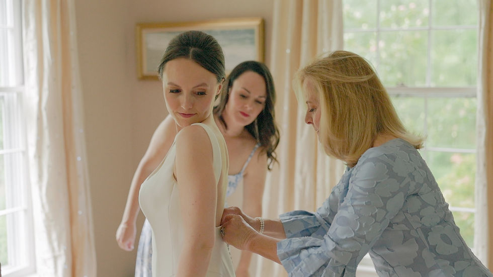 bride getting into her wedding gown with help from her mother and sister