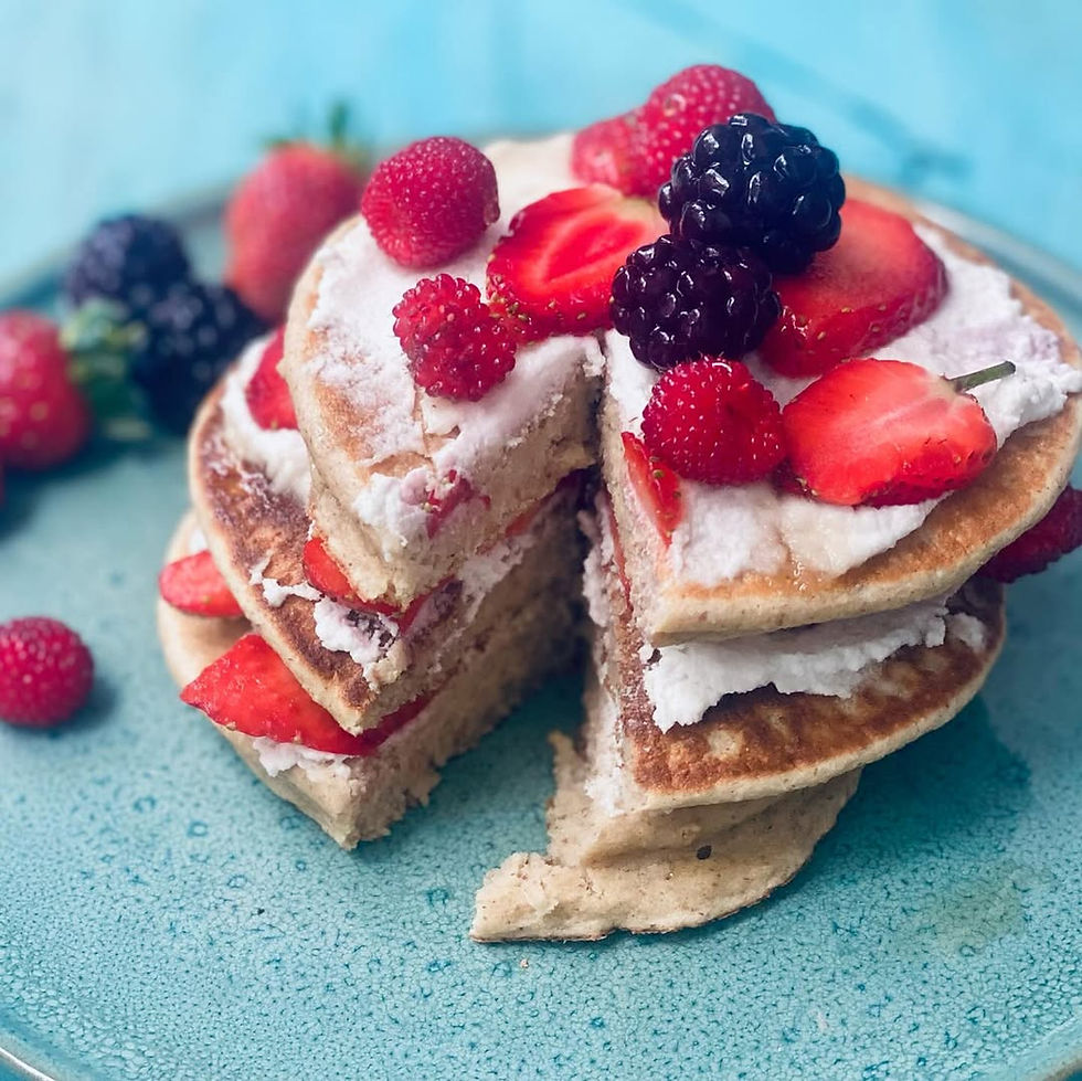 Torre de panqueques con crema y fresas, frambuesas y moras sobre plato azul; una porción está cortada y muestra relleno.