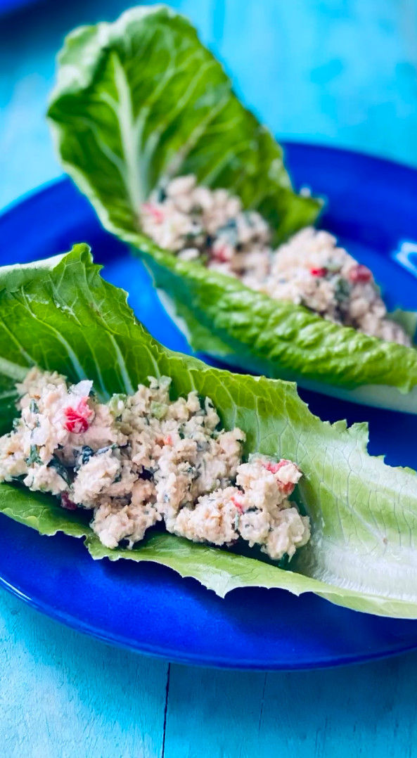 Hojas de lechuga rellenas sobre un plato azul, con una mezcla cremosa y colorida, en una mesa turquesa.