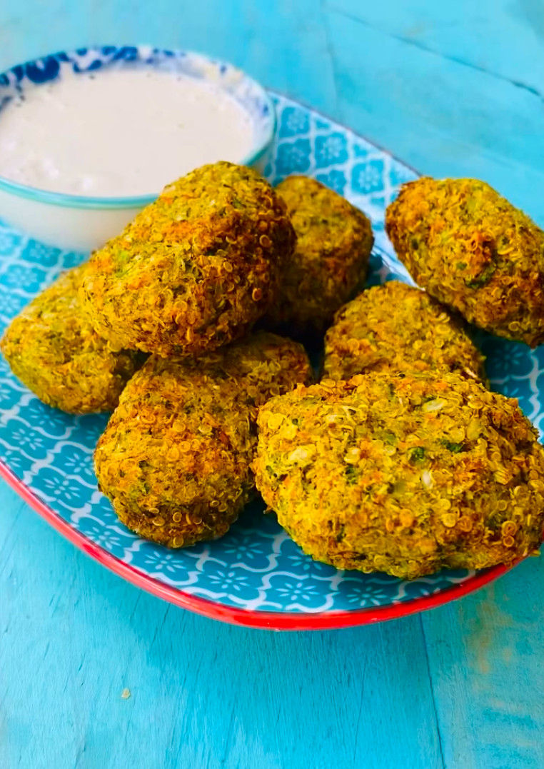 Croquetas de quinoa doradas en un plato azul con salsa blanca, sobre mesa turquesa.