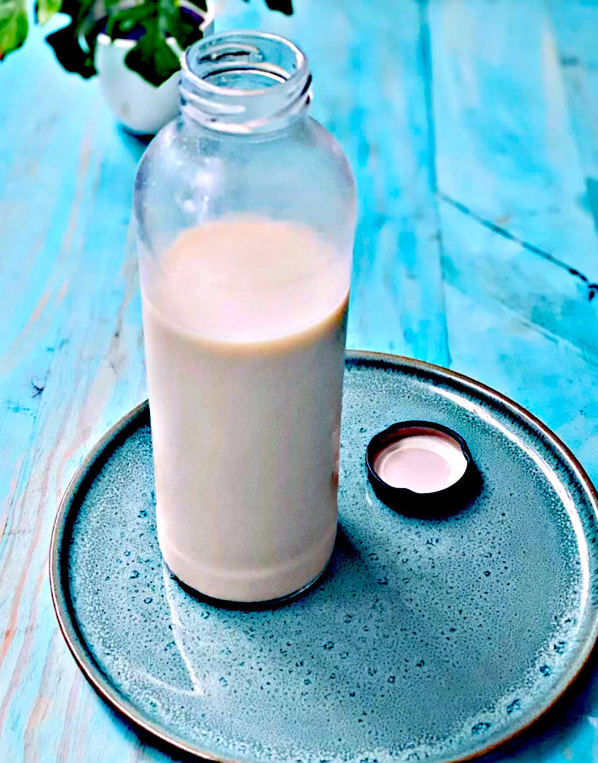 Botella de leche casi llena sobre un plato azul turquesa, con la tapa al lado, en una mesa de madera azul.