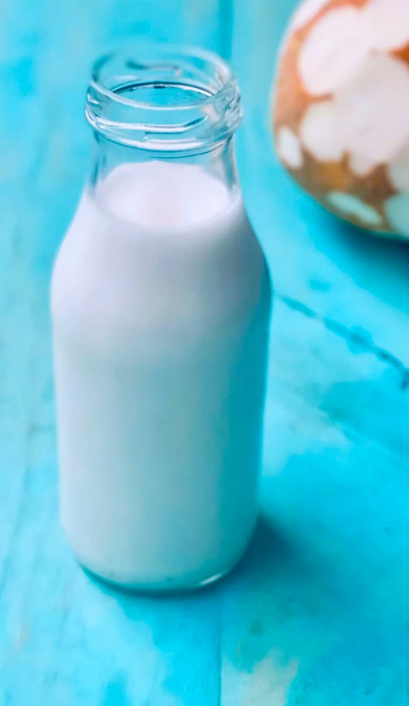 Botella de vidrio con leche sobre fondo turquesa; al fondo, un huevo pintado desenfocado.