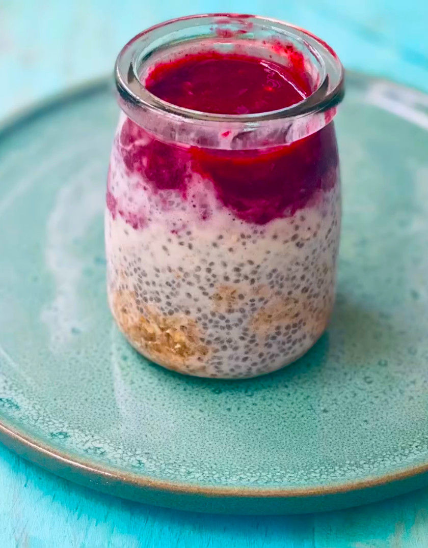 Vaso con pudín de chía y yogur en capas, cobertura magenta de fruta, sobre plato turquesa; imagen fresca y apetitosa