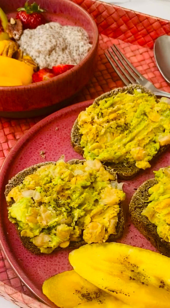 Desayuno en plato rojo: tostadas con aguacate y huevo, mango y fresa, junto a un bol de yogur con chía y fruta.