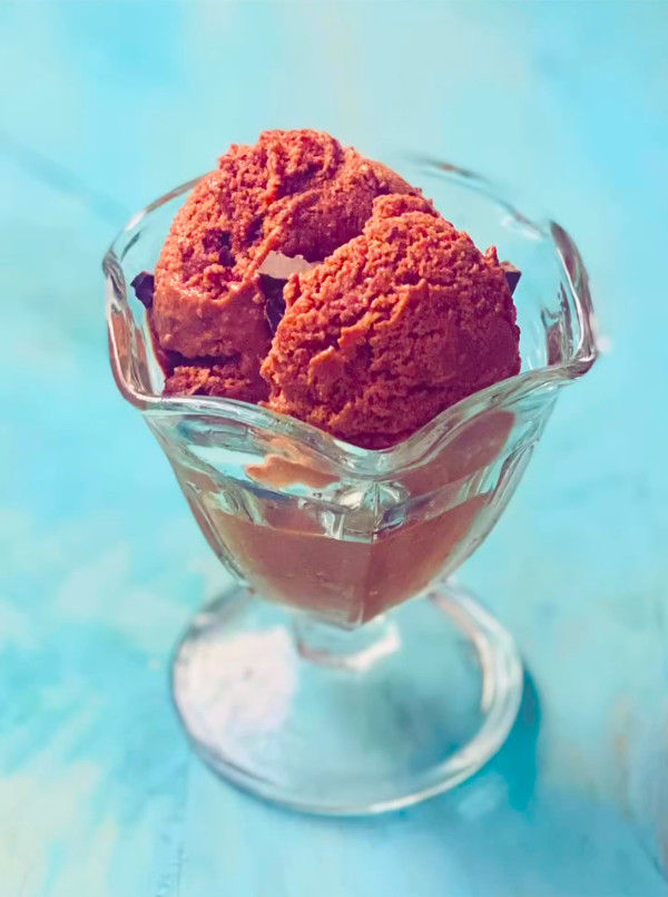 Dos bolas de helado de chocolate en copa de cristal sobre fondo azul, con aspecto cremoso y apetitoso.