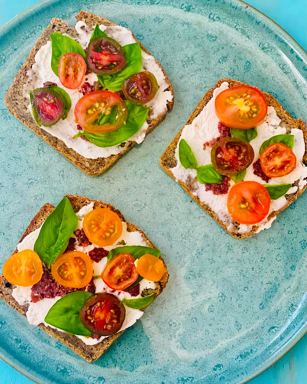 Tres tostadas con queso, tomates cherry y albahaca sobre un plato turquesa.