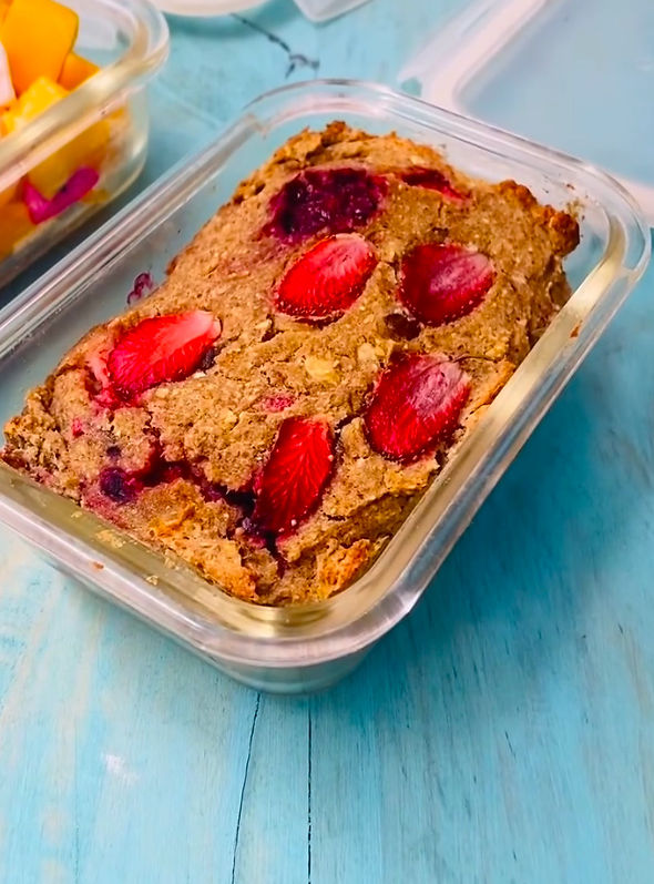 Bizcocho de fresa en recipiente de vidrio sobre mesa azul, con otro envase de fruta al fondo.