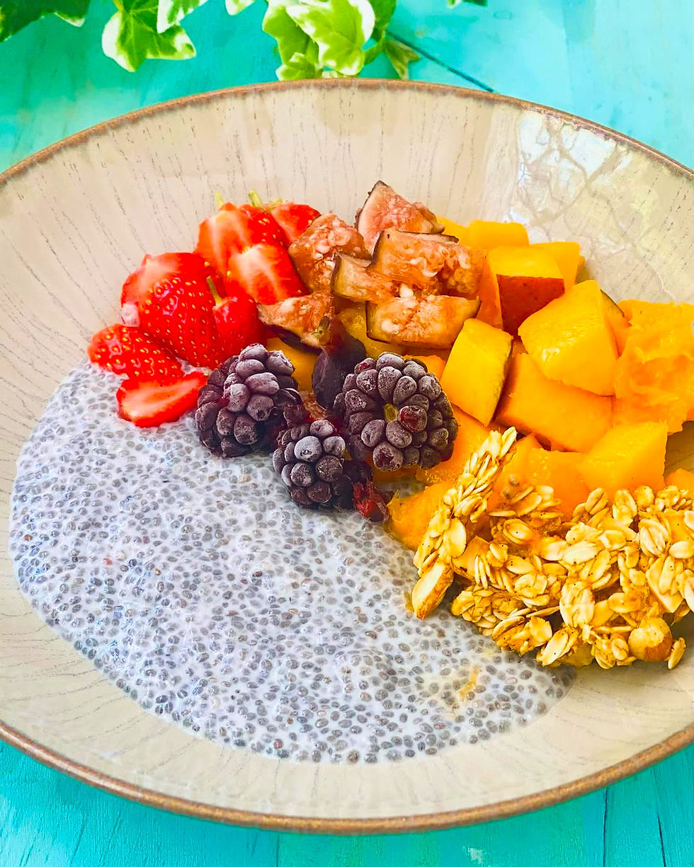 Bowl de pudín de chía con fresas, moras, mango, higos y granola sobre mesa turquesa.