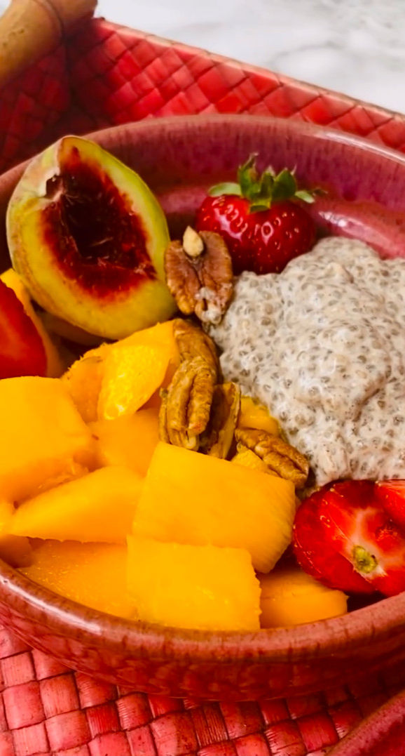 Bol con mango, fresa, durazno, nueces y pudín de chía sobre mantel rojo; colores vivos y aspecto fresco.