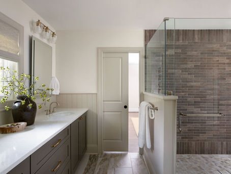 Modern bathroom with glass shower, wood cabinets, and a white countertop. A vase with green branches adds a touch of nature. Neutral tones.