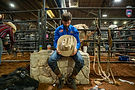 A bull rider sits holding his hat inside the rodeo arena