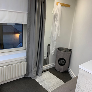 Cozy treatment area with a changing space enclosed by a curtain, a window with a blind, and a laundry basket in the newly renovated skincare salon.