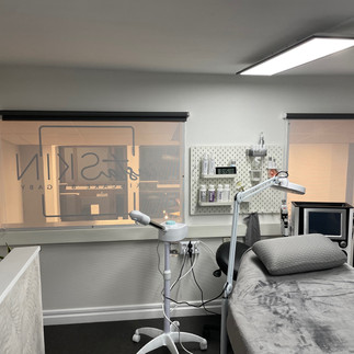 After renovation: Modern skincare treatment room with a comfortable treatment bed, medical equipment, and a large window displaying the InstaSkin logo in the renovated salon.