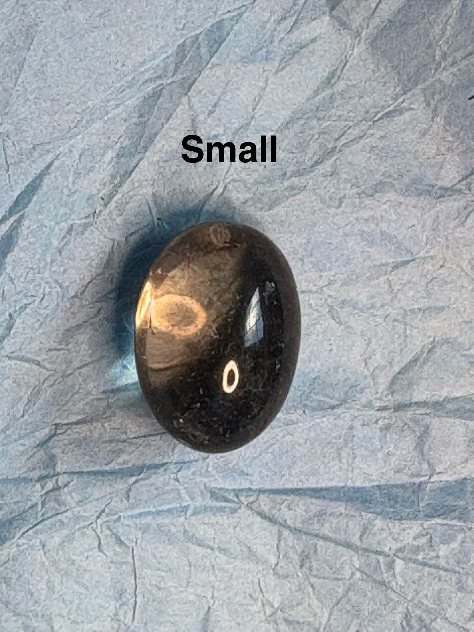 Small, black stone with a unique pattern, Hare Carving Small on blue paper.