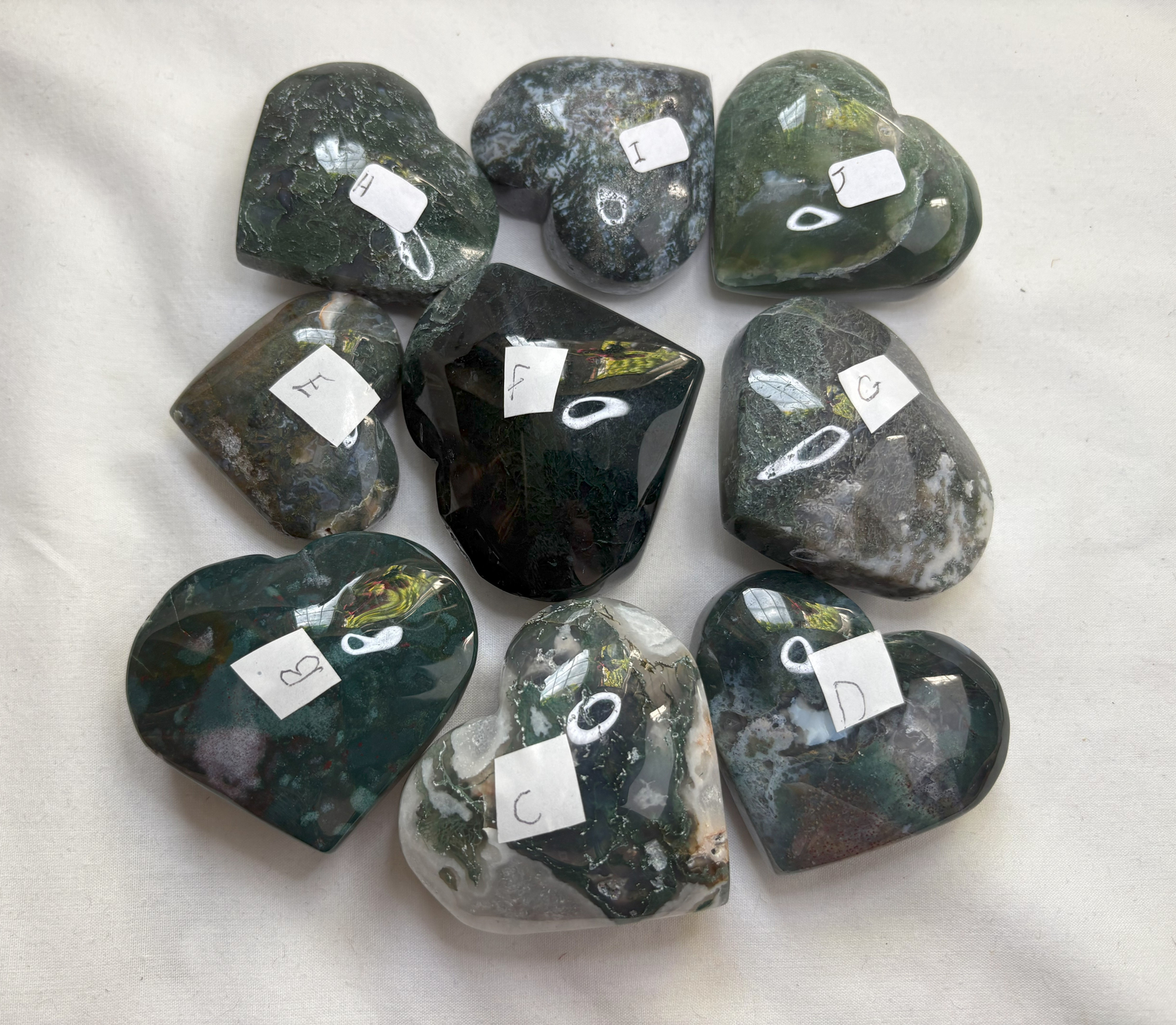 Nine heart shaped stones with price tags, sparkle in stone, on white surface.