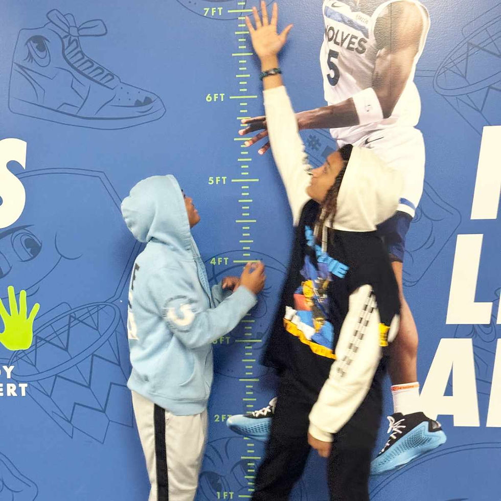 Brothers stand next to a wall with a life-size diagram of Anthony Edwards of the Minnesota Timberwolves.