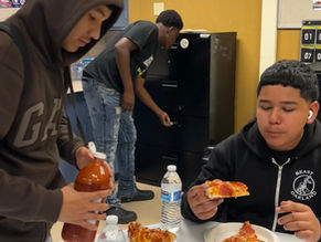 Students enjoying pepperoni pizza with Valentina hot sauce and grabbing additional snacks in the IYT Room snack cabinet, sharing laughs and building community.