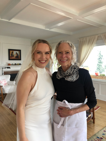 Beautiful bride in white halter dress smiles with woman in apron.