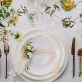 White plate setting with peach ribbon, small flowers, and gold cutlery.