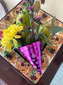 A Mardis Gras themed party hat full of yellow and purple flowers on a decorative plate. 