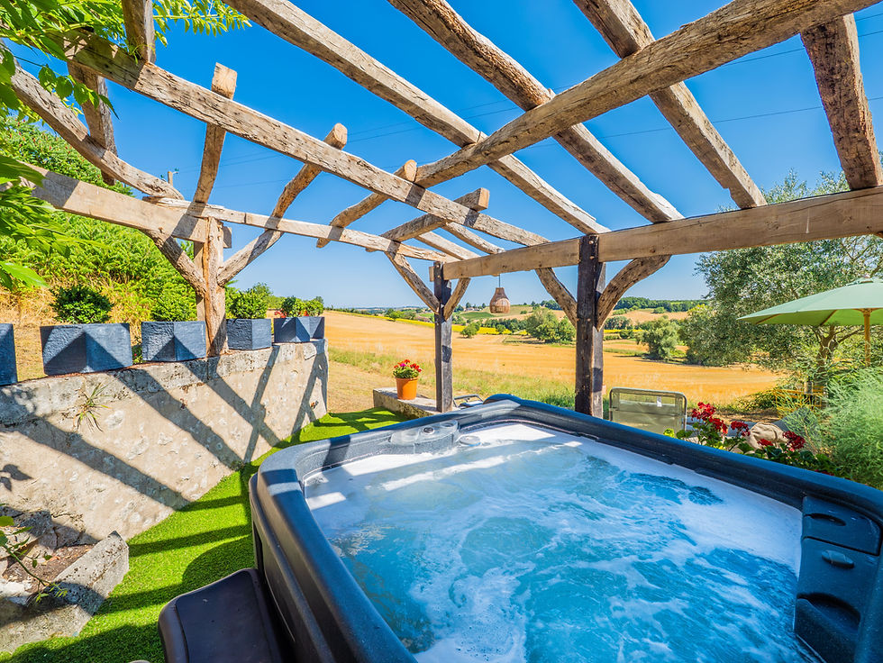 Outdoor hot tub under a wooden pergola with field views.