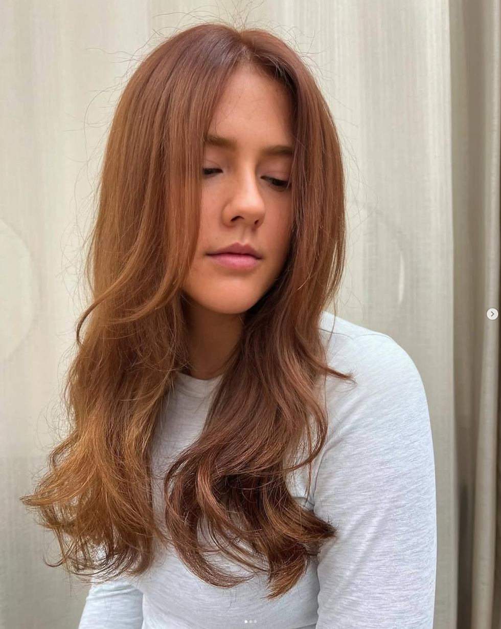 Soft copper brown hair with long layers, styled smooth with natural movement and shine.