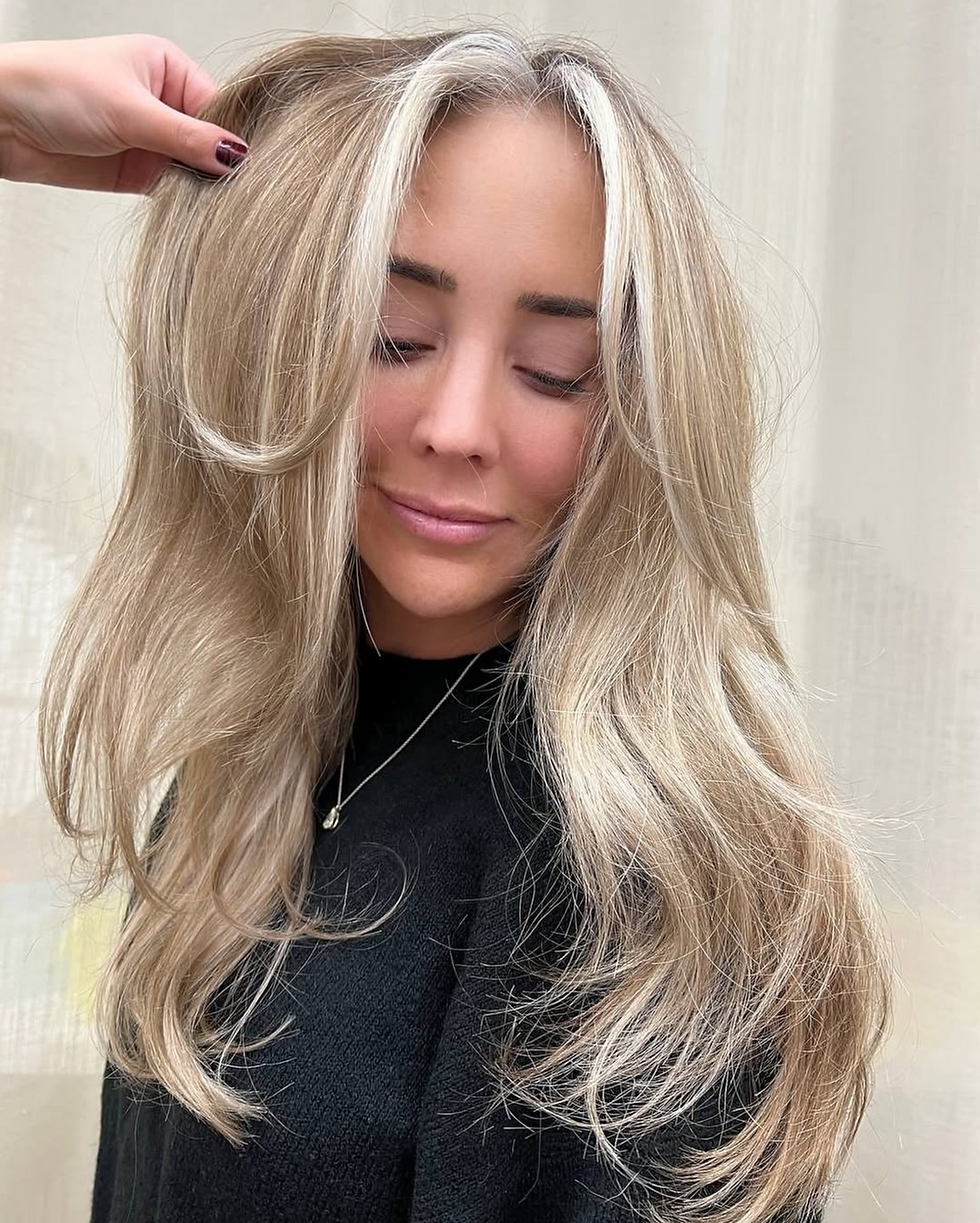 Cool beige blonde balayage with face-framing layers, styled in soft waves for a voluminous finish.